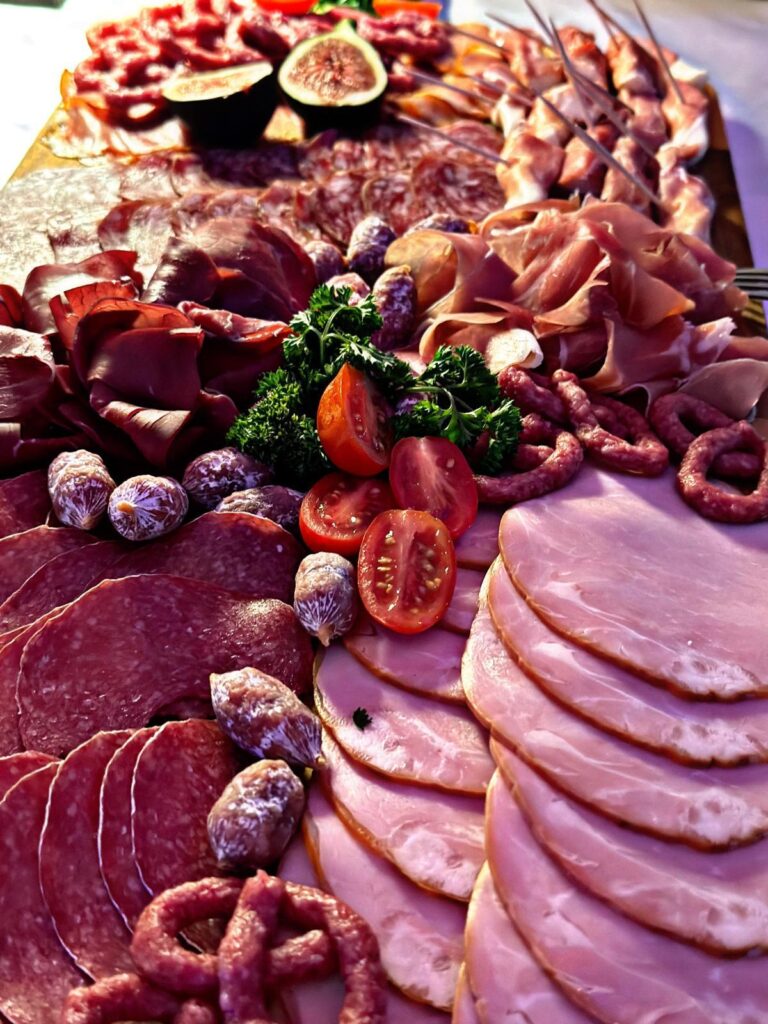 Ein Charcuterie-Brett mit verschiedenen Aufschnitten, Mini-Würstchen, Kirschtomaten, Feigen, frischer Petersilie und Wurstwaren, kunstvoll auf einer Holzunterlage angerichtet